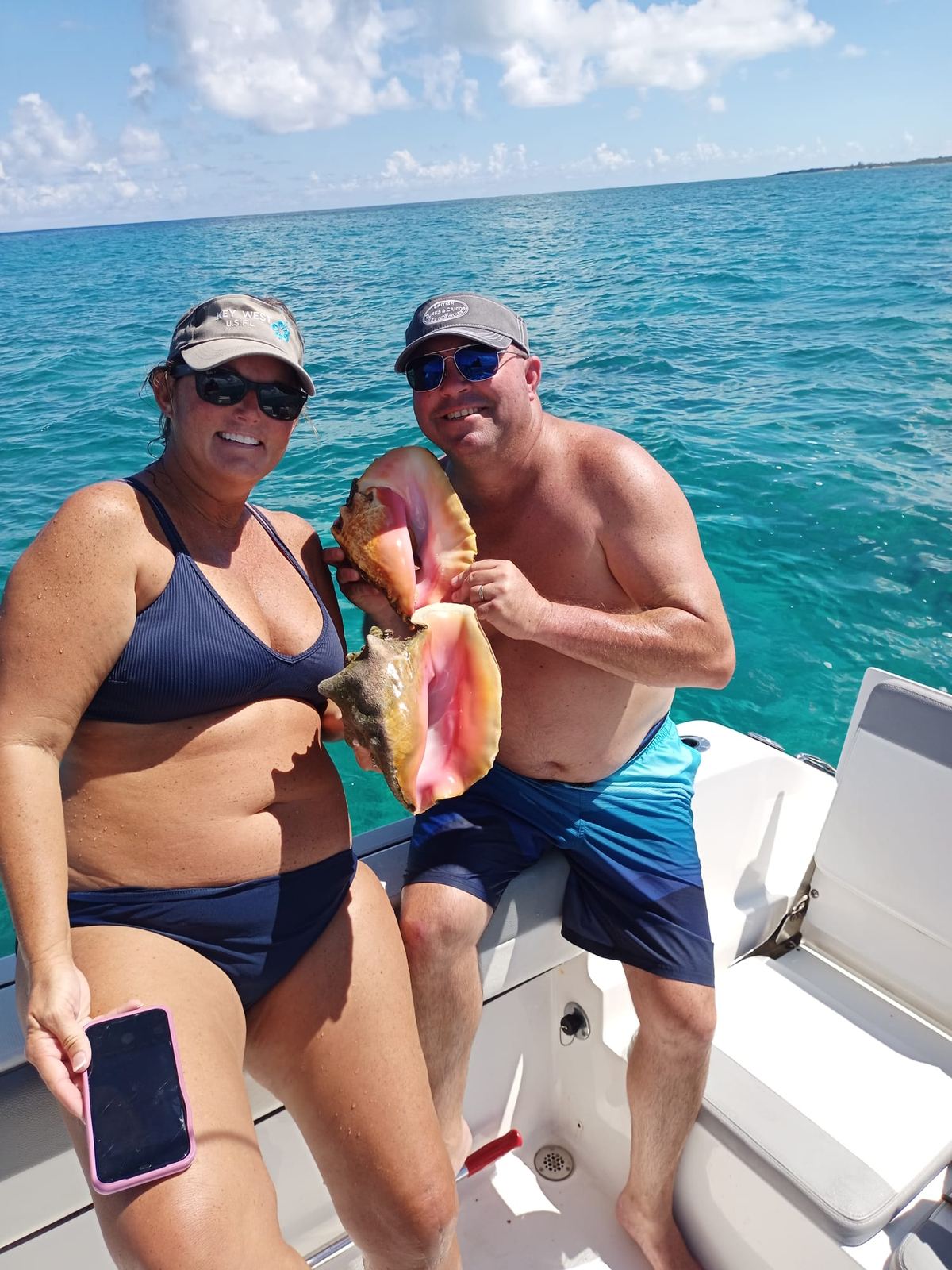Couple holding pink conch shells on the boat